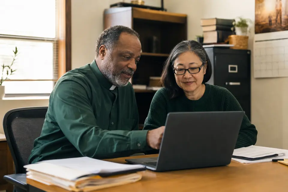 Pastor and volunteer treasurer check an online application status in a church office.