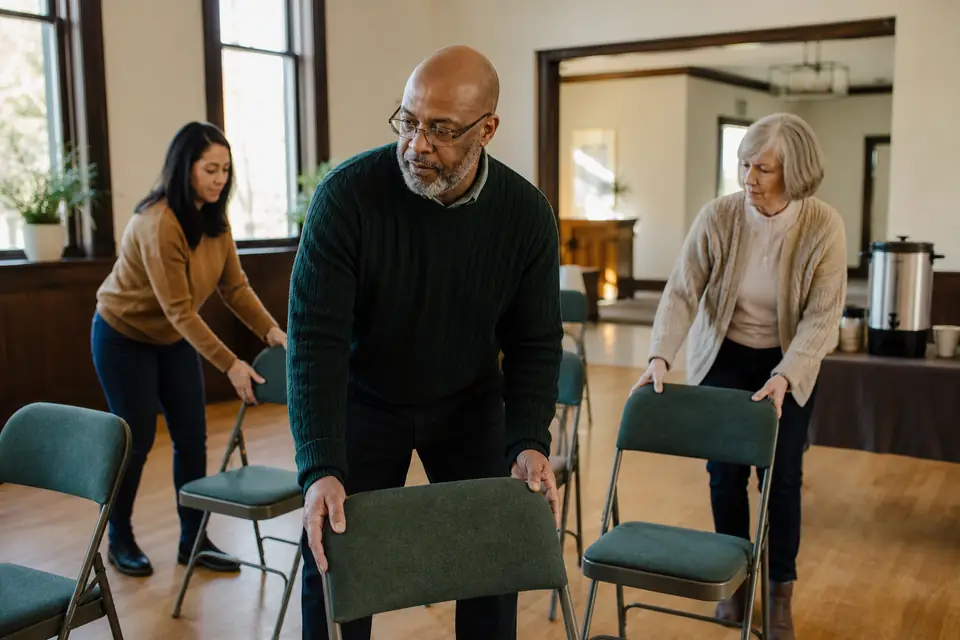 Pastor and congregation volunteers setting up folding chairs in a church fellowship hall