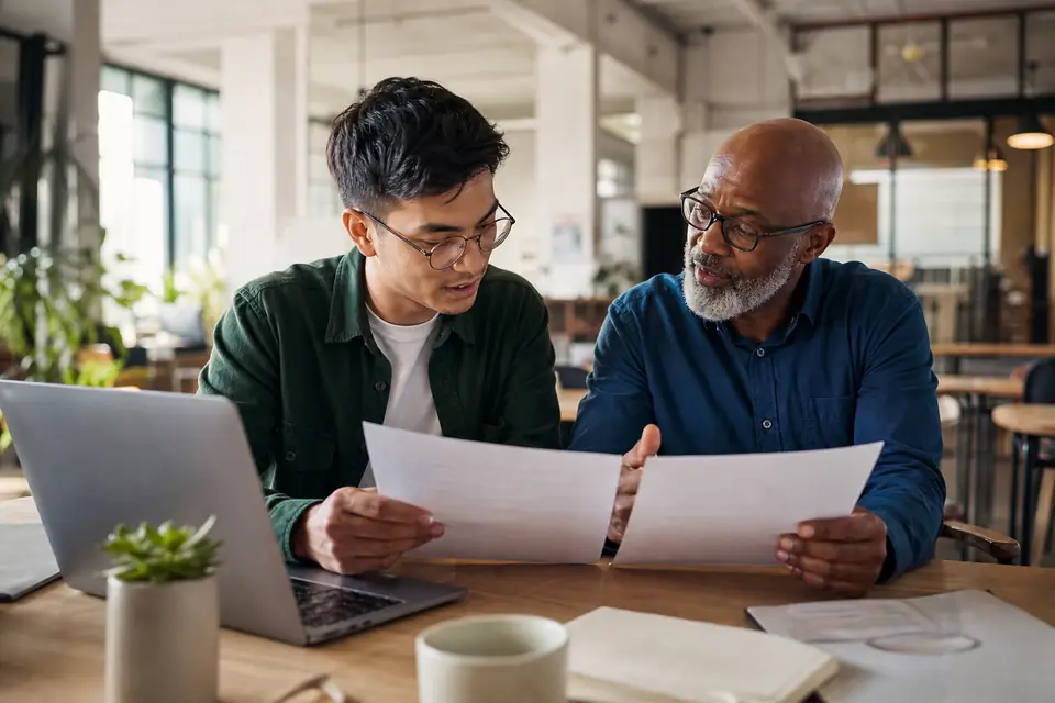 Two people compare printed application checklists at a co-working space desk.