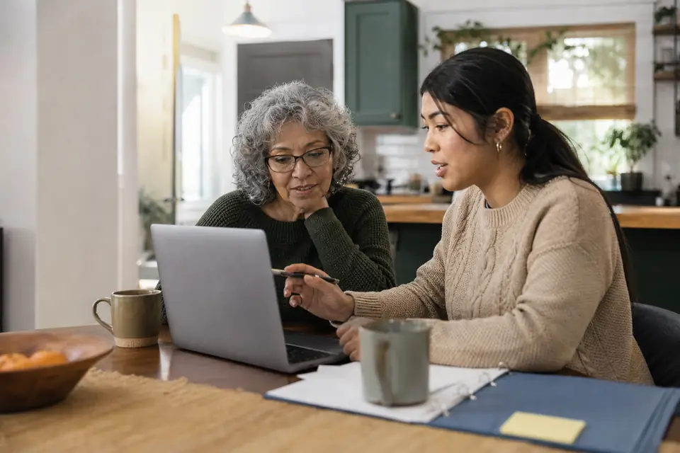 Two volunteers of different generations planning a nonprofit at a kitchen table with a laptop.