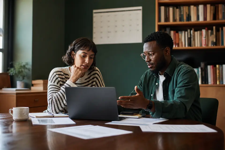 Two nonprofit board members comparing notes on a laptop in a library meeting room